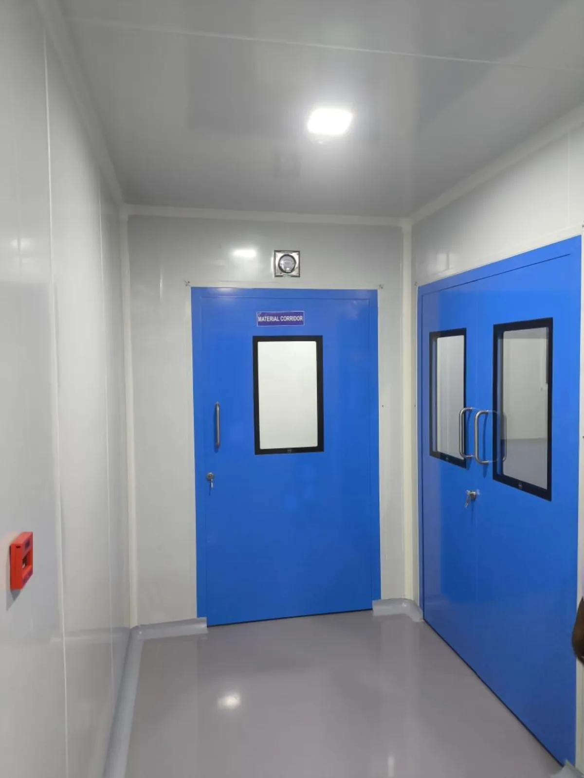 Cleanroom material corridor with blue controlled door, vision panel, differential pressure gauge above the frame and coved skirting